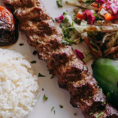 A close-up of a lamb kebab with rice and salad on a plate.