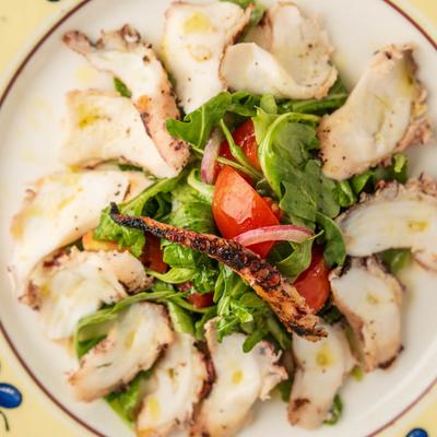 Grilled octopus surrounding an arugula salad.