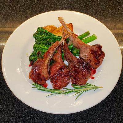 Grilled lamb chops served with broccolini and roasted potatoes, garnished with rosemary.