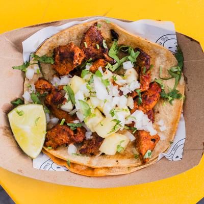 Mexican taco al pastor served in a cardboard with a lime wedge.