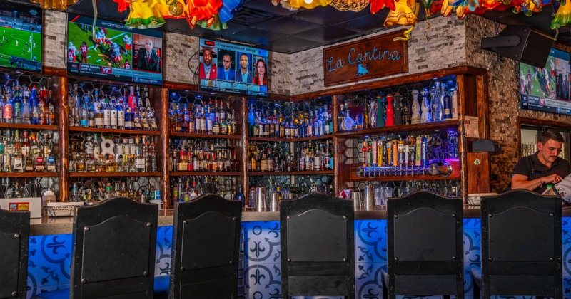 Interior of a colorful bar with liquor bottles, TVs, and vibrant glass light fixtures