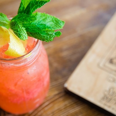 Partial view of a pink craft cocktail with a lime peel and a mint sprig.