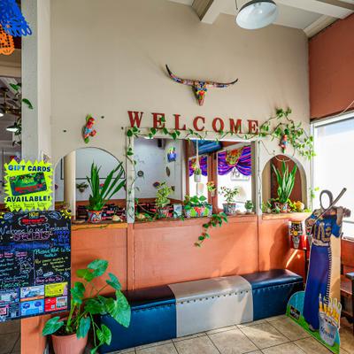 Interior of a Mexican restaurant with a welcome sign, potted plants, and colorful decorations.