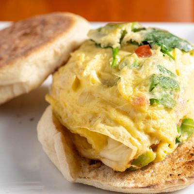 Breakfast sandwich with scrambled egg, bacon, cheddar, spinach, and red peppers.