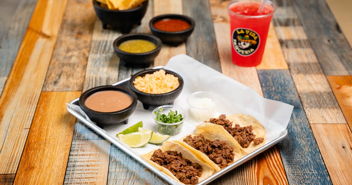 Beef street tacos served with rice, refried beans, cilantro, lime wedges, and a red drink