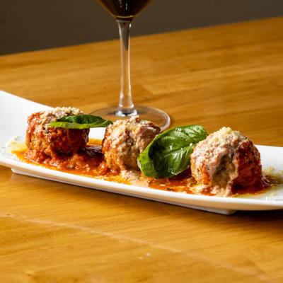Meatballs topped with tomato sauce, grated cheese, and fresh basil leaves.