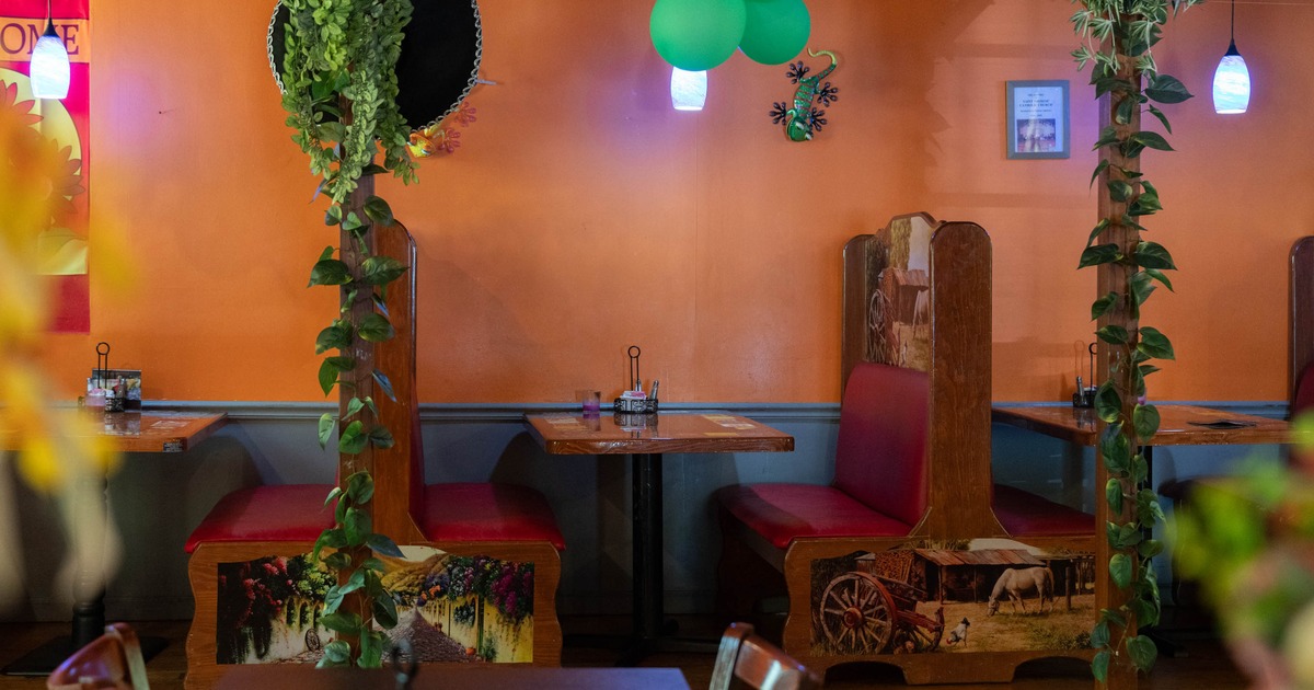 Interior of a colorful restaurant with orange walls, decorated booths, and indoor plants