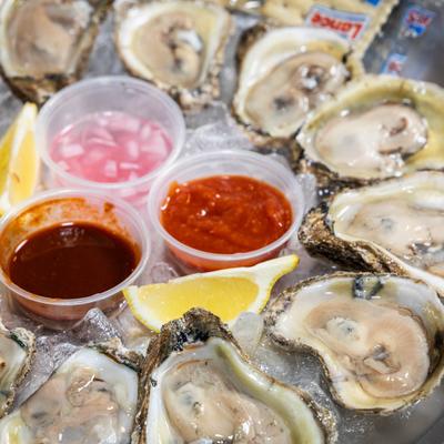 Raw oysters served on a bed of crushed ice with cocktail sauce, mignonette, and lemon wedges.
