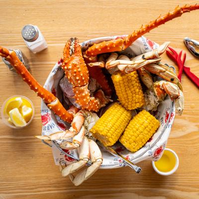 Seafood boil dish featuring king crab legs and corn on the cob served in a metal bucket.