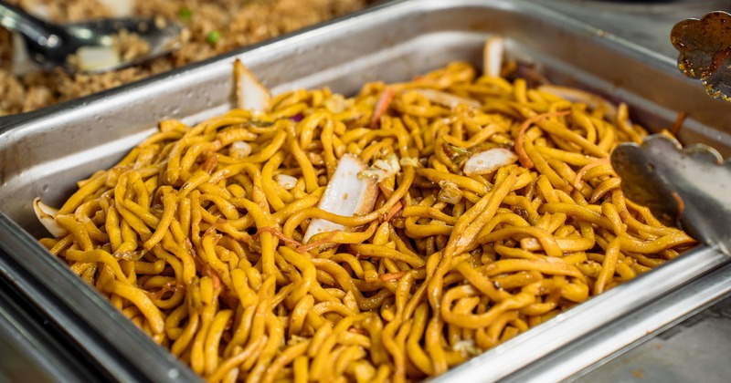 A metal buffet tray filled with thick, stir-fried yellow Chinese noodles