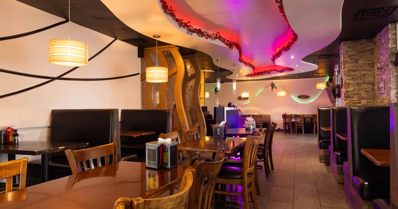 Interior of a restaurant with wave-like ceiling, ambient lighting, booths, and tables