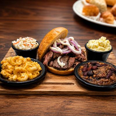 Smoked steak sandwich with side dishes.