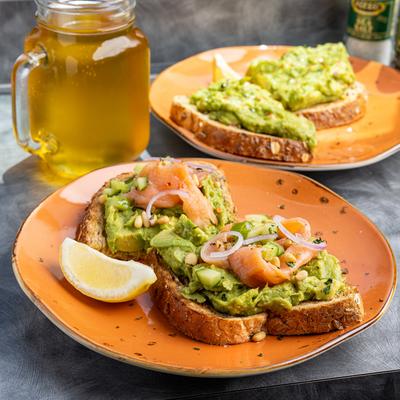 Avocado toast topped with smoked salmon and pickled onions, served with lemon wedge.