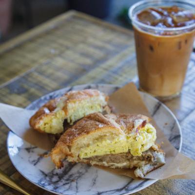 Croissant breakfast sandwich srerved on the table with iced coffee.