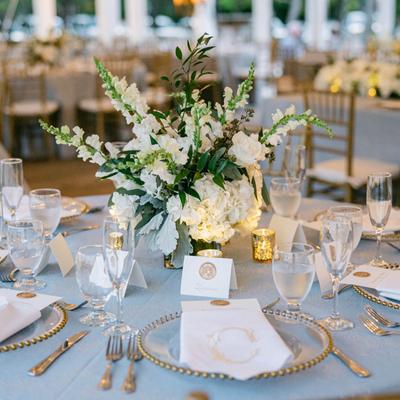 Elegant table setting  with white floral centerpiece, glassware, gold accents, and soft candlelight.