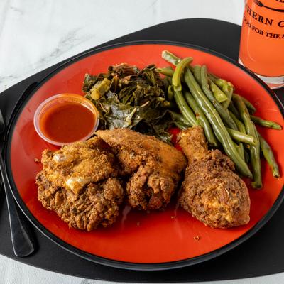 Three pieces of fried chicken served with collards, green beans and sauce.