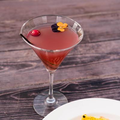 Cocktail served in a martini glass, garnished with a cranberry and a flower.