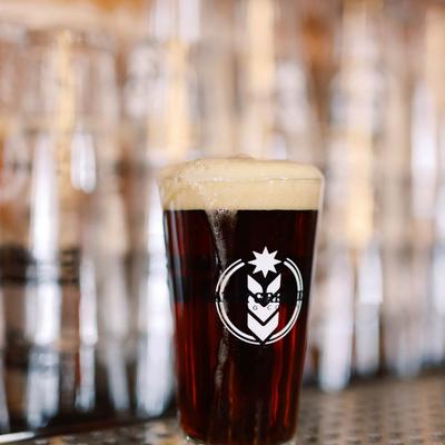 Dark beer with a foamy head in a branded pint glass at a bar counter.