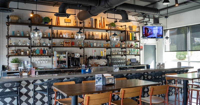 Modern bar interior with wooden tables, bar stools, shelves with liquor bottles