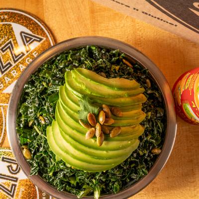 A kale salad bowl topped with sliced avocado and pumpkin seeds.