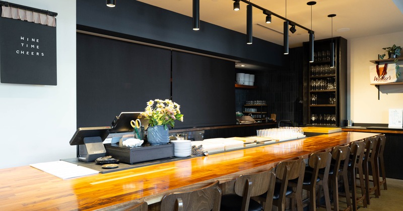 Warmly lit wine bar - a long wooden counter, bar stools, hanging lights, flower arrangement