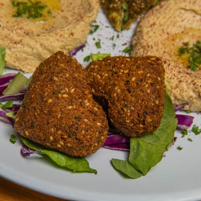 Hart-shaped falafel serevd on a plate with hummus and fresh vegetables, close-up.