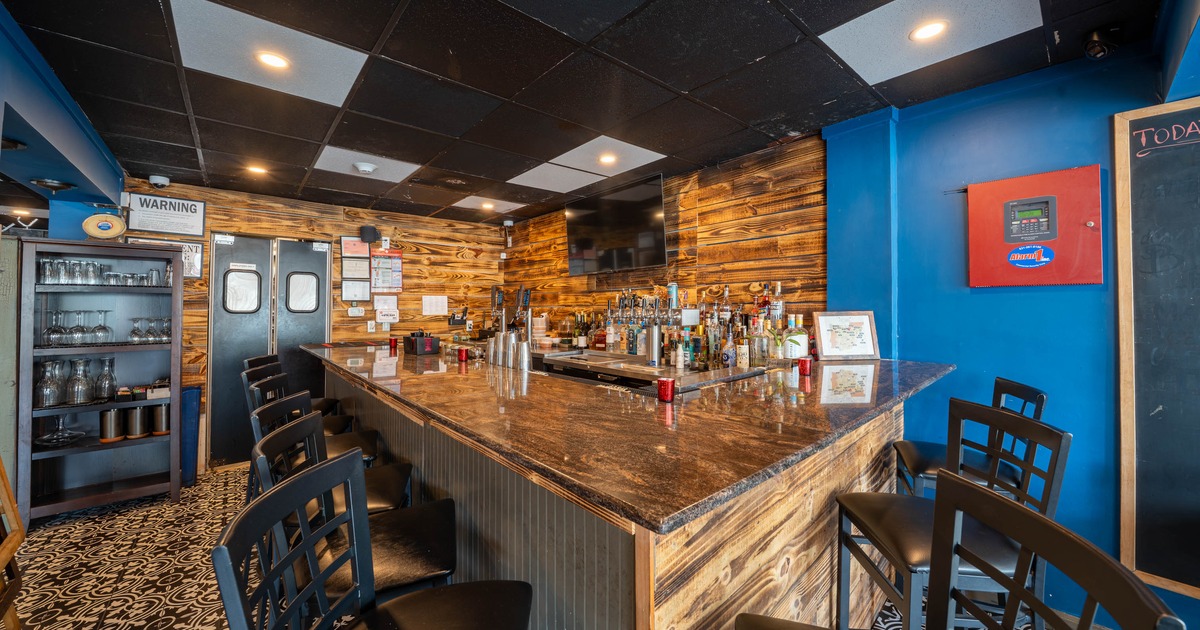 Interior of a bar with a polished stone counter, wooden panels and a shelf of liquor bottles