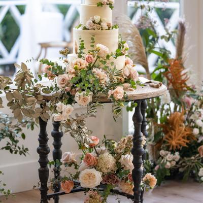 A wedding cake adorned with pastel roses and greenery sits on a rustic table indoors