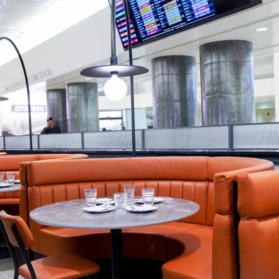 A restaurant booth with orange leather seating, a round table set with glasses and cutlery.