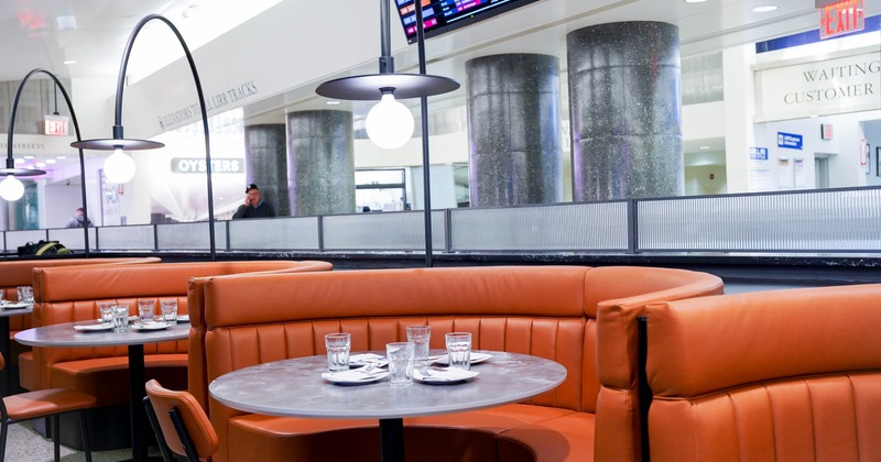 A restaurant booth with orange leather seating, a round table set with glasses and cutlery