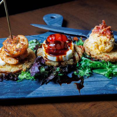 Fried green tomato flight, served with three distinct toppings on a blue board.