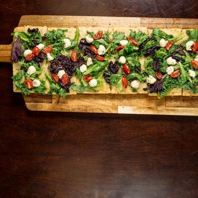Italian flatbread toped with greens, mozzarella, and cherry tomatoes, served on a wooden board.