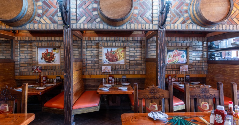 Interior view of a rustic restaurant featuring brick walls, wooden booths with orange cushions