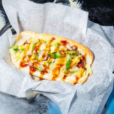 Hawaiian dog topped with diced pineapple, peppers, onion and a sauce drizzle.