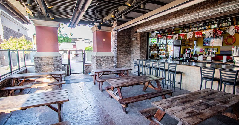 Covered patio area, conjoined wooden tables and benches, bar