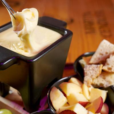 Cheese Fondue in a black bowl served with small bowls of croutons, apples, and pretzels.