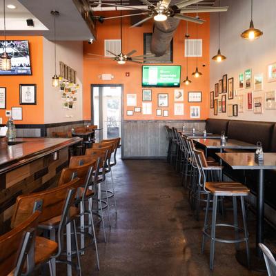 Interior, bar and bar chairs, banquette seating by a wall, walls decorated with pictures.