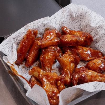 Black takeout tray filled with glossy reddish-brown sauced chicken wings on printed paper..