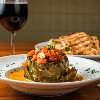 Stuffed artichoke with tomatoes and herbs served with a glass of red wine.