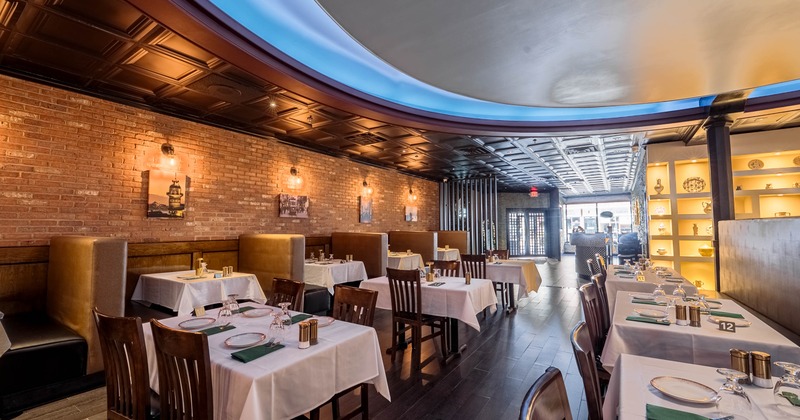 Interior of a warmly lit restaurant with brick walls, booths, and tables with white tablecloths