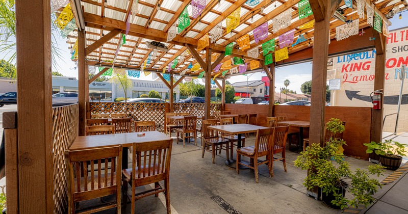Outdoor, dining area with wooden tables, chairs, and colorful papel picado banners overhead