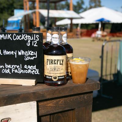 Exterior, a bar table with bourbon, a mixed drink, and a cocktail menu on it.