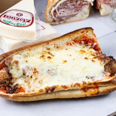 Chicken Parmesan sandwich with Asiago cheese wedges nearby.