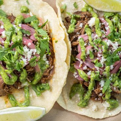 Smoked brisket tacos topped with greens and pickled onions.
