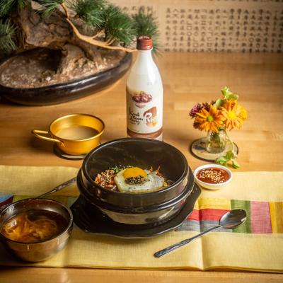 Bulgogi Bibimbap dish with sides and bottle of rice vine on the table.
