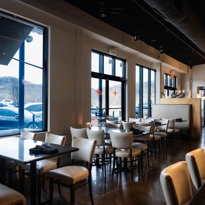 A restaurant interior featuring tables and chairs arranged near large windows.