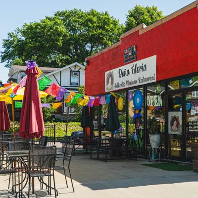 Storefront with signage and entrace and outdoor seating with umbrellas and colorful banners.