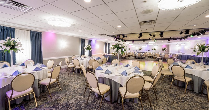 An elegantly decorated banquet hall with round tables, floral centerpieces, and blue napkins
