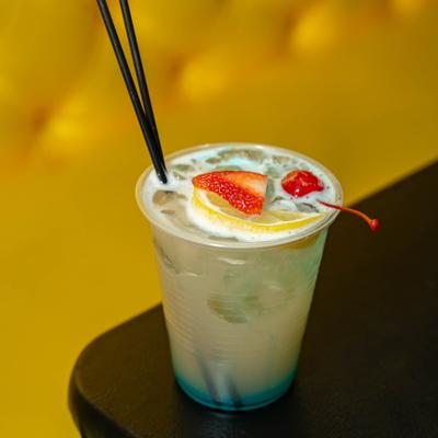 Cocktail drink served in a plastic cup with fruit garnish.