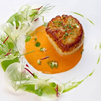 Seared scallop served over creamy orange sauce with herbs.